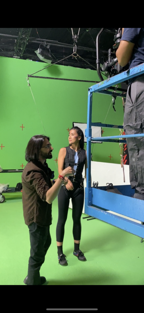 Julia on set, standing in front of a green screen and tied into a rig